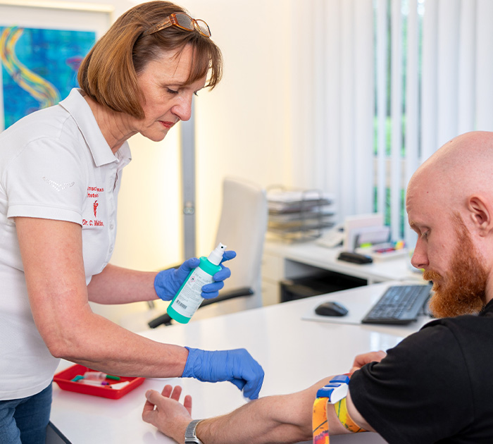 Eine freundlich blickende Frau mit kurzen braunen Haaren desinfiziert den Arm eines Mannes